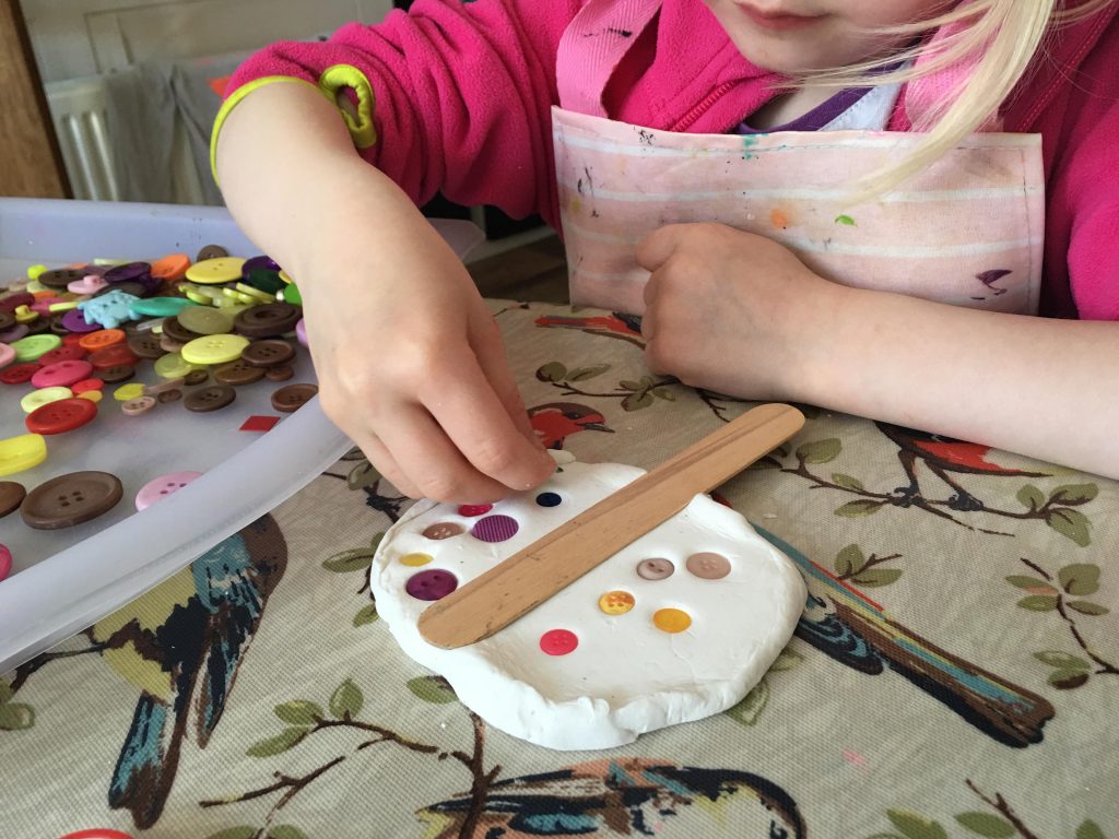 child pressing buttons into clay
